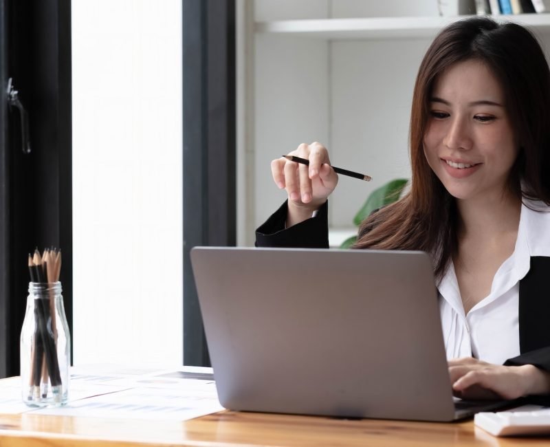 Business asian woman using laptop for do math finance on wooden desk in office, tax, accounting