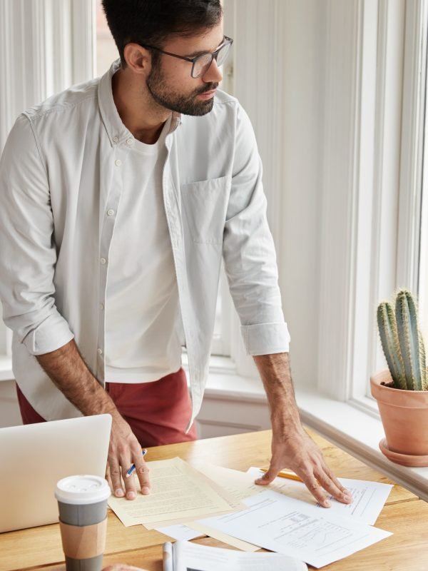 Vertical shot of male coworker cant make right accountings in papers, looks at documents planner, st