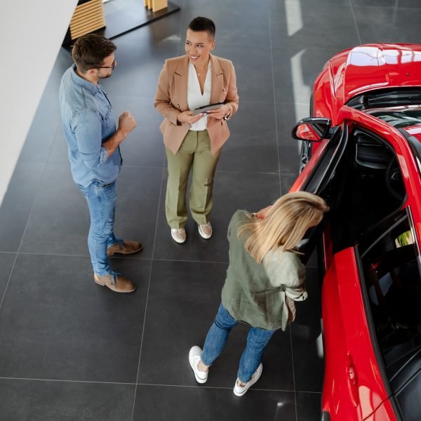 couple choosing and buying car at car showroom. Car saleswoman helps them to make right decision.