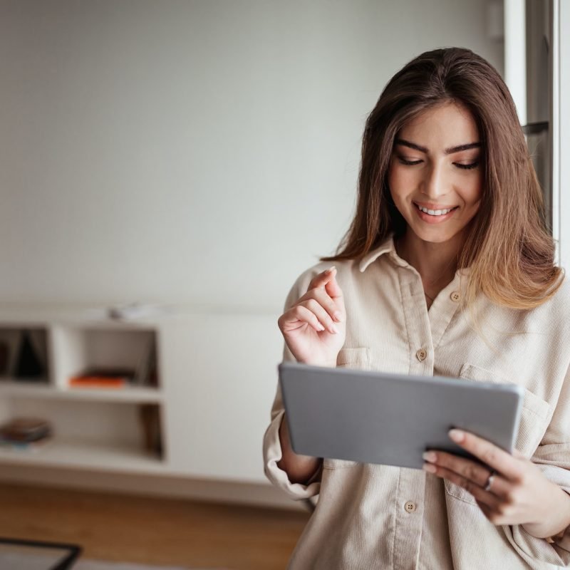 Smiling pretty young asian lady in casual use tablet for control smart home, enjoy study and work