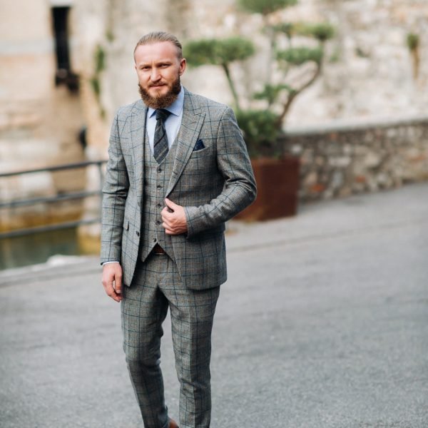 A man with a beard in a strict grey three-piece suit with a tie in the old town of Sirmione, a