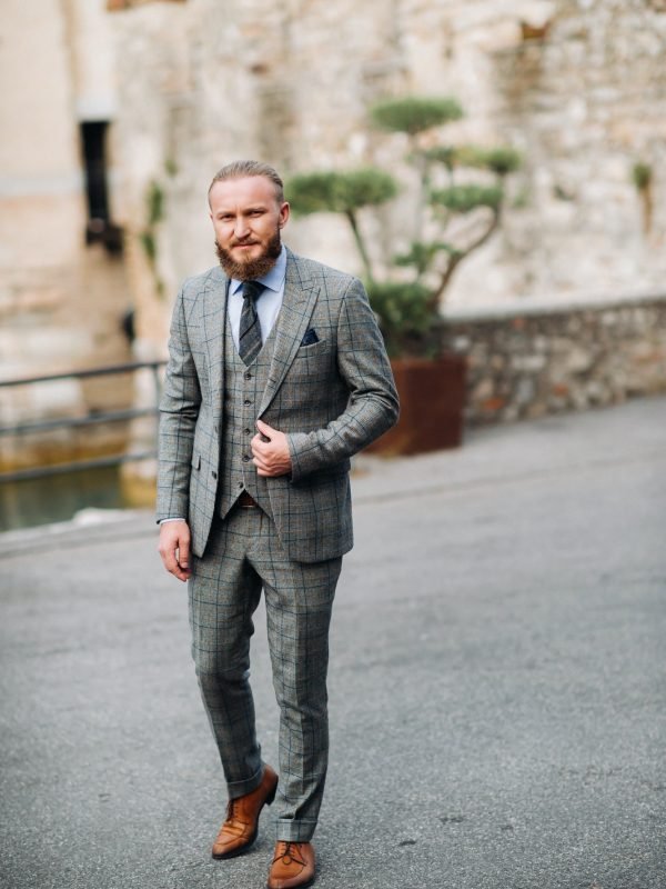 A man with a beard in a strict grey three-piece suit with a tie in the old town of Sirmione, a