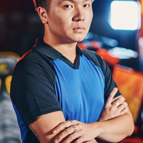 Vertical shot of young asian guy, male cyber sport gamer keeping arms crossed and looking at camera