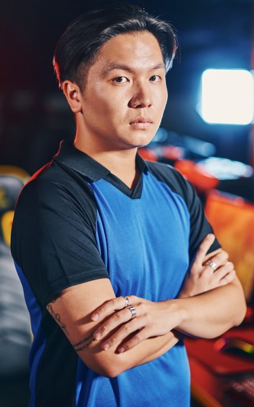 Vertical shot of young asian guy, male cyber sport gamer keeping arms crossed and looking at camera