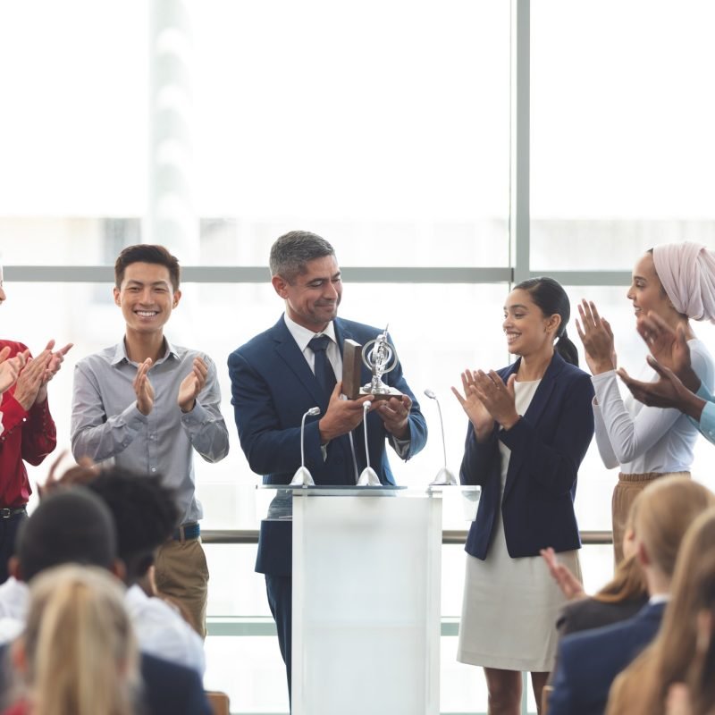 Businessman holding award on podium with colleagues at business seminar