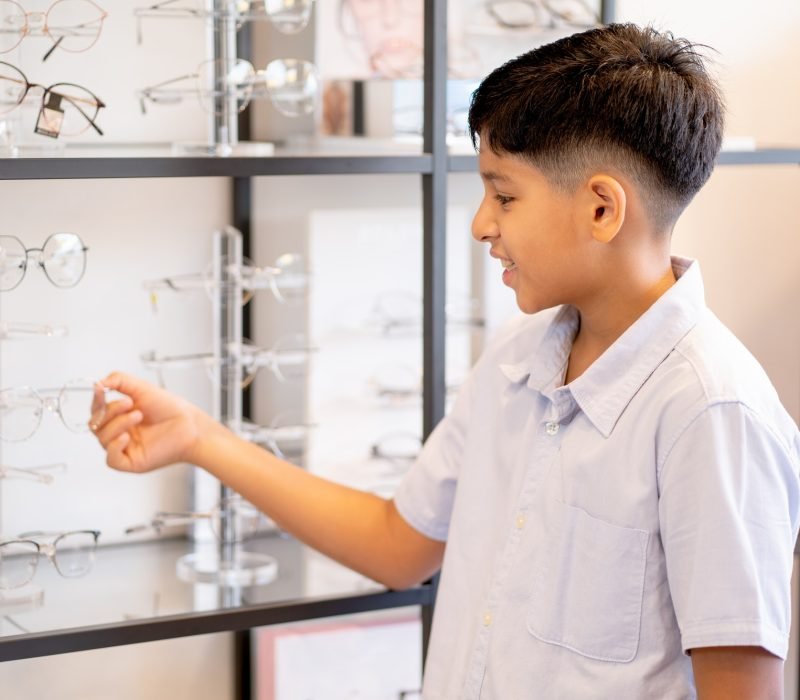 Indian boy hold glasses on shelf during selection to buy some products for his eyecare