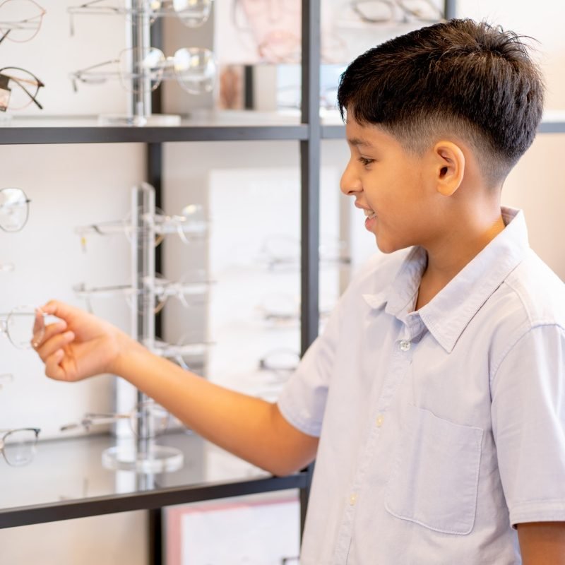 Indian boy hold glasses on shelf during selection to buy some products for his eyecare