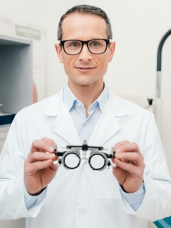 portrait of optometrist in white coat holding trial frame in hands in clinic
