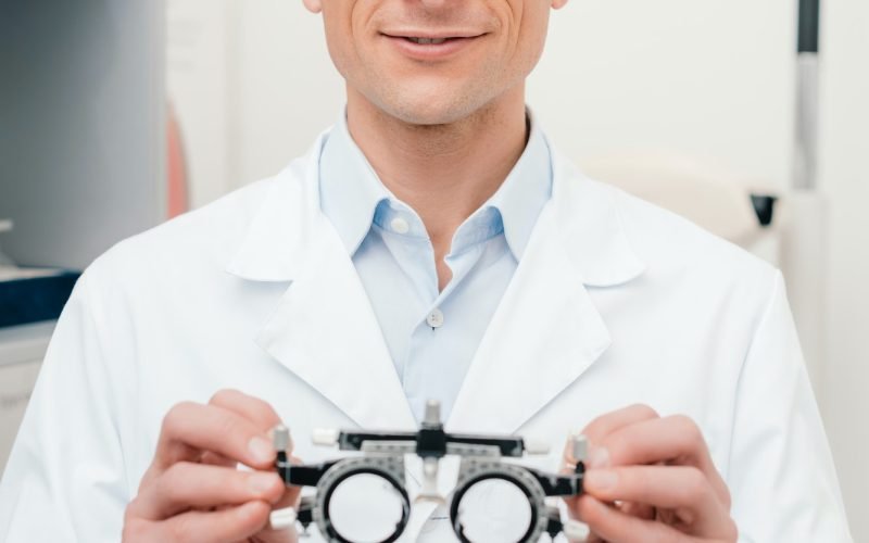 portrait of optometrist in white coat holding trial frame in hands in clinic
