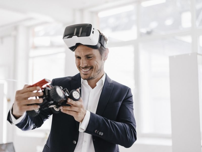 Smiling businessman wearing VR glasses looking at toy racing car