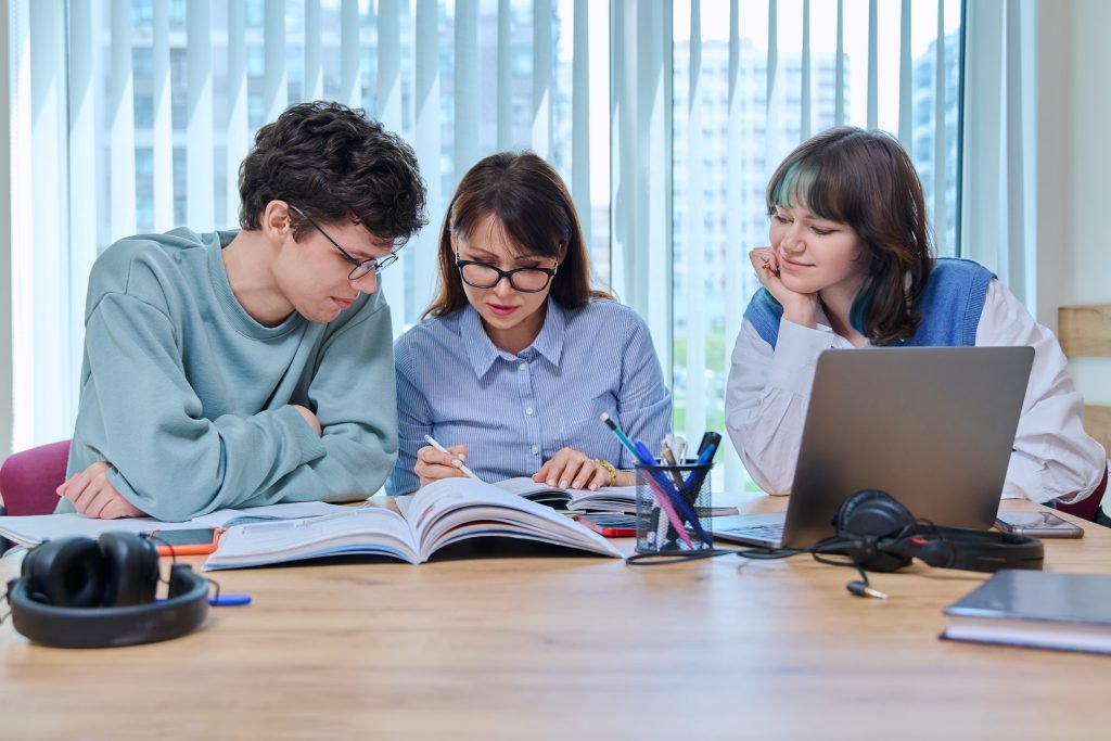 College students with teacher sitting at desk in classroom studying languages, sciences