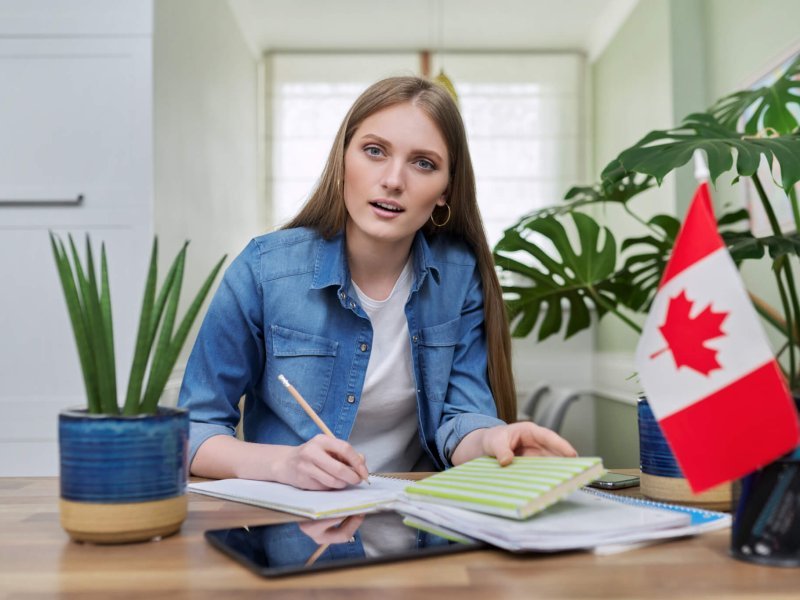 Online training, female teenager sitting at home looking at webcam, Canadian flag on table