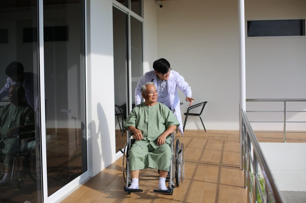 Caretaker Helping Senior Man with Disability at Checkup Visit