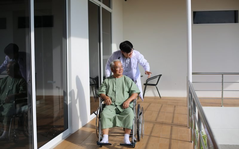 Caretaker Helping Senior Man with Disability at Checkup Visit
