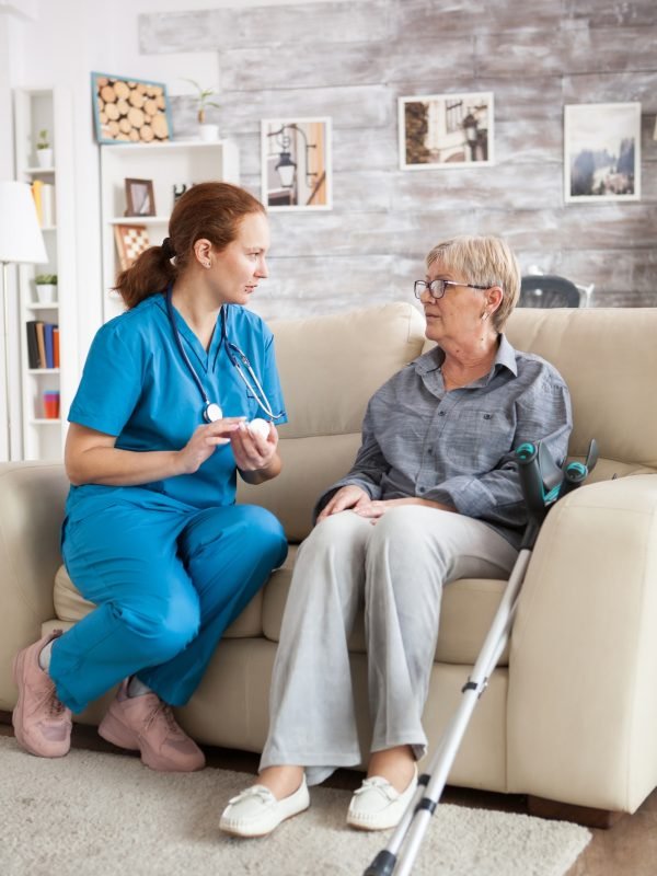 Female nurse sitting on couch with senior woman
