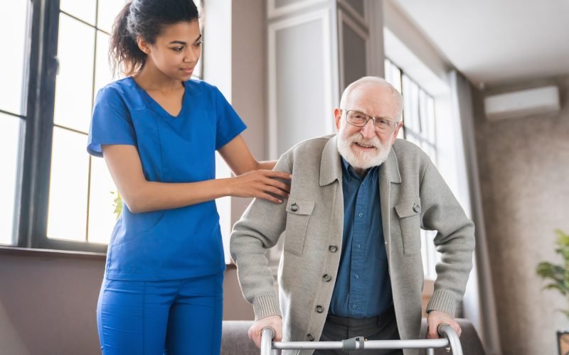 Handicapped man using walker - rehabilitation at home. Nurse helping disabled man using walker
