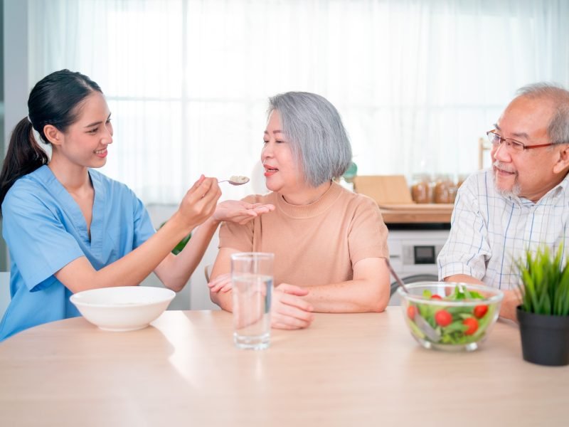 Nurse or doctor who work as homecare staff help to serve a spoon of mush rice to senior woman
