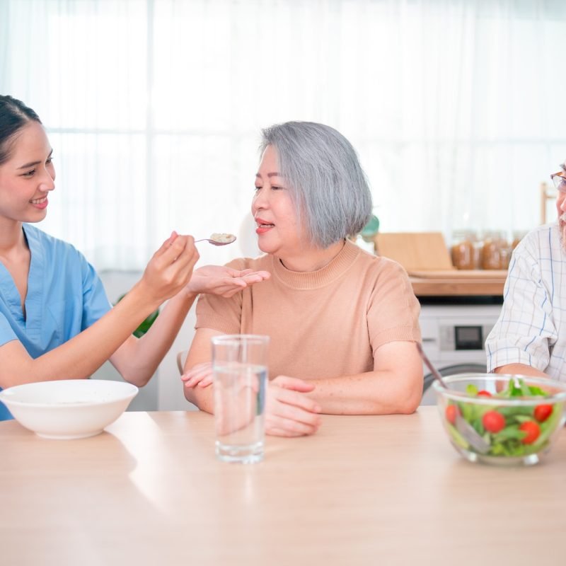 Nurse or doctor who work as homecare staff help to serve a spoon of mush rice to senior woman