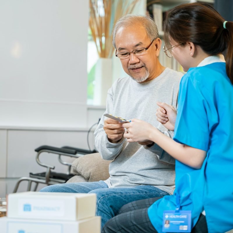 Woman nurse caregiver showing prescription drug to senior man at nursing home