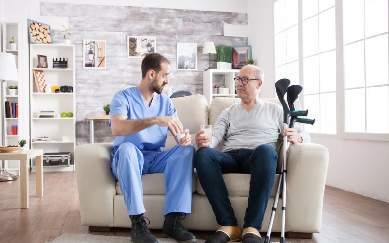 Young male nurse in nursing home with pills for senior man