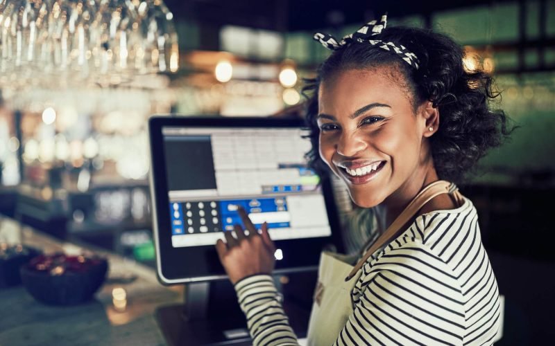 smiling-african-waitress-using-a-restaurant-point-of-sale-terminal