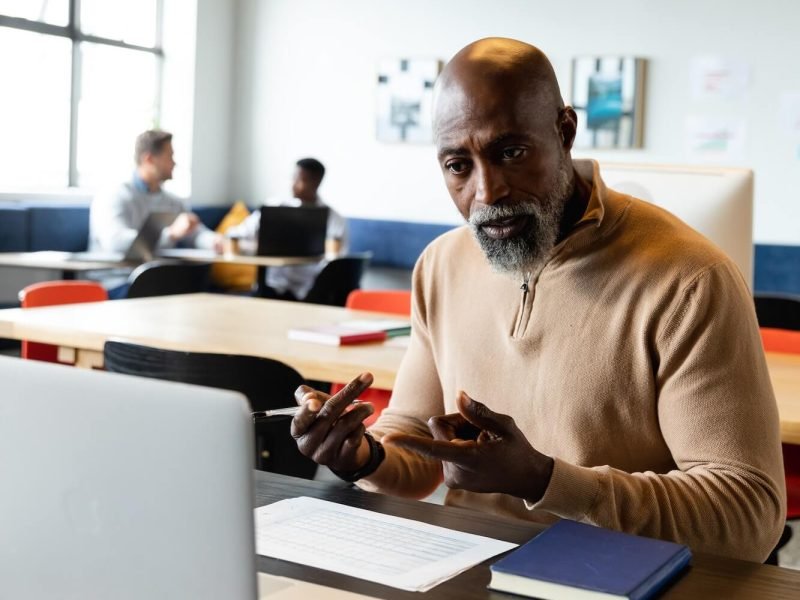 African american mature businessman video calling through laptop in creative office