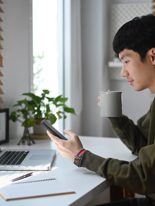 Side view of young businessman drinking coffee an checking social media on mobile phone.